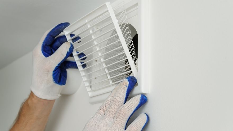 Instalator nakłada kratkę wentylacyjną na kanał w ścianie