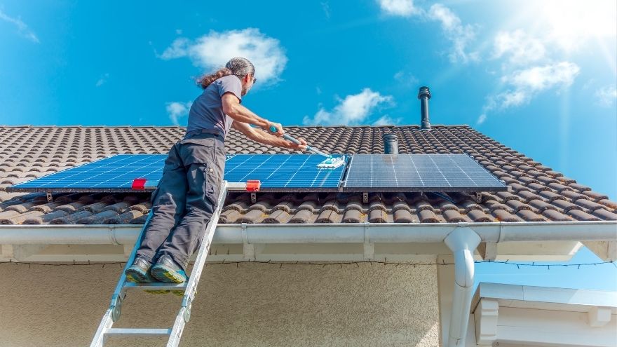 Instalator czyści panele fotowoltaiczne na dachu domu jednorodzinnego