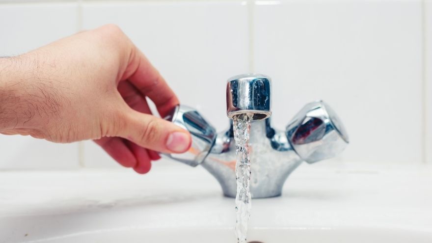 Mężczyzna odkręca wodę z kranu baterii termostatycznej w łazience na umywalce