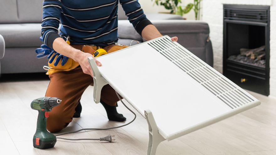 Instalator naprawia grzejnik elektryczny na kabel w salonie domu jednorodzinnego