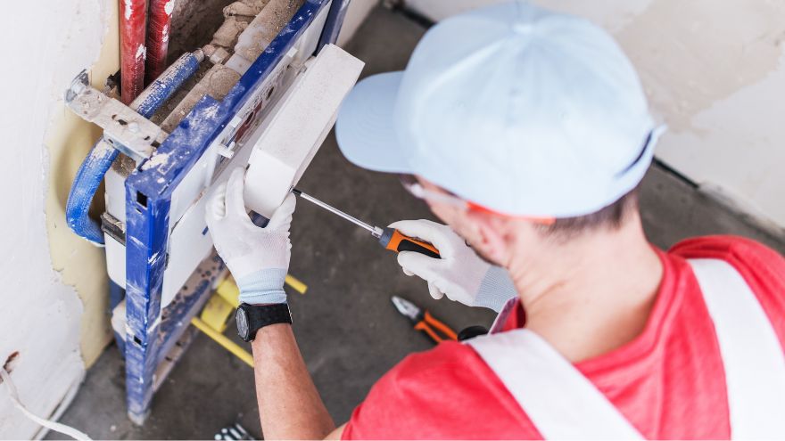 Instalator montuje stelaż podtynkowy na ścianie w łazience