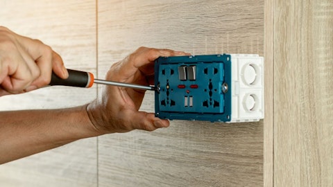 Instalator montuje gniazdko elektryczne natynkowe na drewnianej ścianie