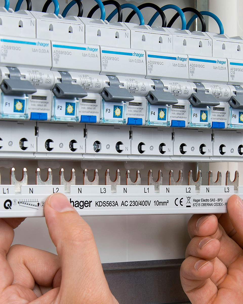 Ręce montujące szynę grzebieniową do zestawu wyłączników nadprądowych i różnicowoprądowych w rozdzielnicy elektrycznej
