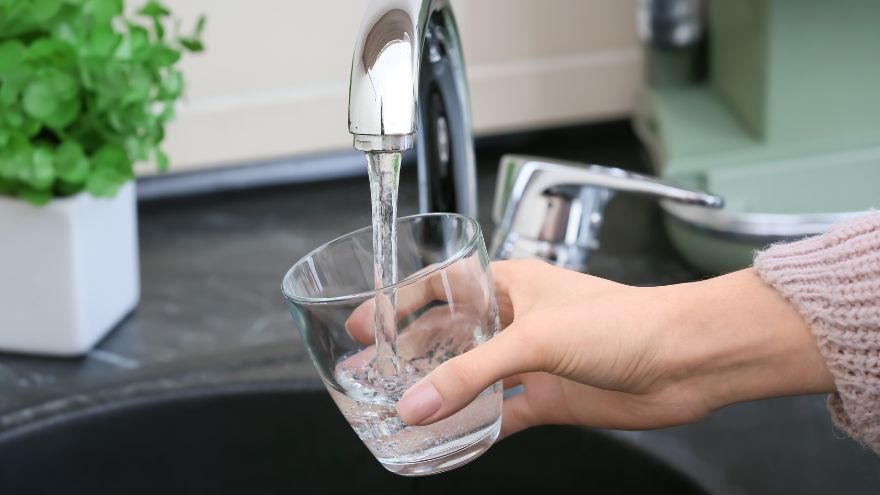 Dłoń trzymająca szklankę która napełnia się wodą z kranu