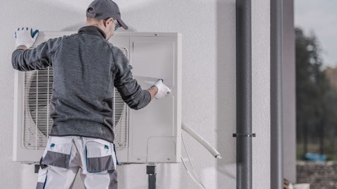 Instalator montujący pompę ciepła przy ścianie budynku