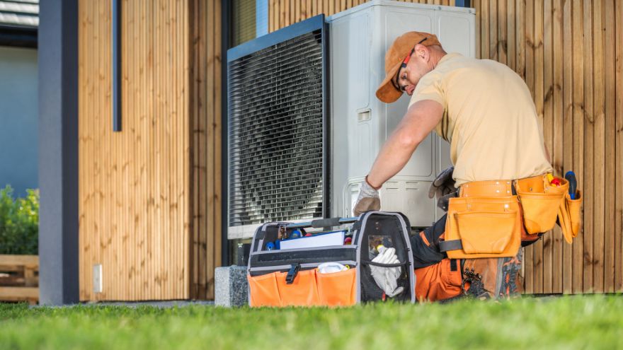Instalator naprawiający pompę ciepła przy kt&oacute;rej leży skrzynka z narzędziami