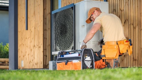 Instalator naprawiający pompę ciepła przy której leży skrzynka z narzędziami