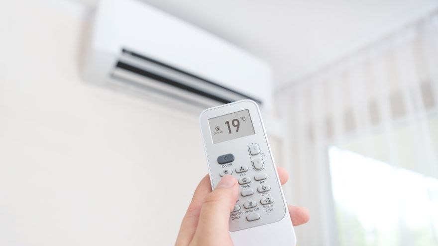 Pilot od klimatyzacji trzymany w ręku na tle klimatyzatora