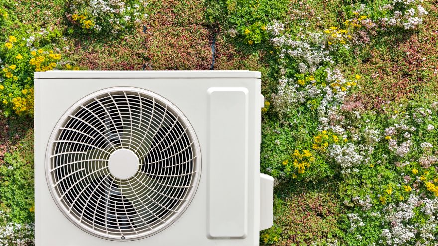 External heat pump unit against a backdrop of a green, blooming wall