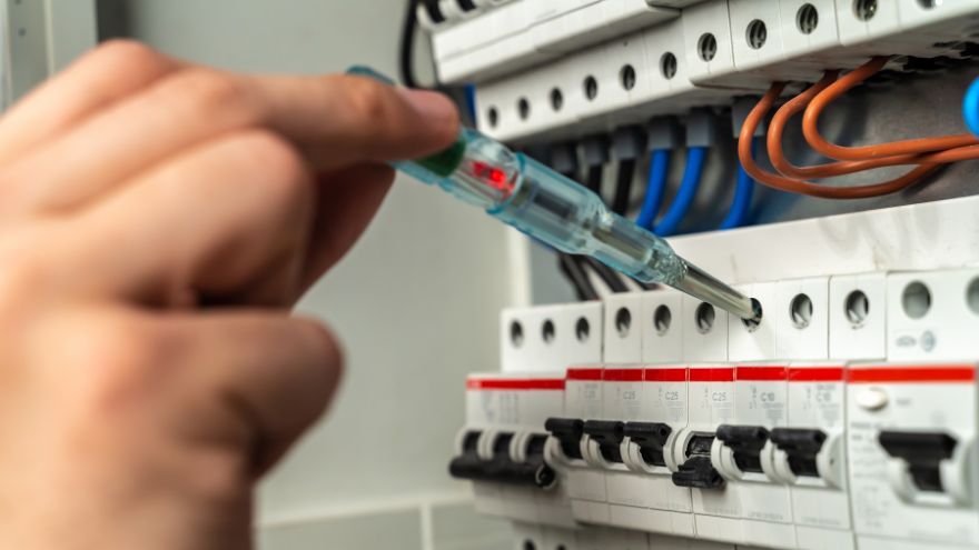 Elektryk sprawdza napięcie pr&oacute;bnikiem w skrzynce z bezpiecznikami
