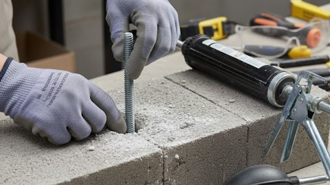 Ręce w rękawiczkach osadzające kotwę chemiczną w betonie