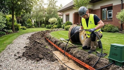Pracownik układający kabel telekomunikacyjny w wykopie w ogrodzie