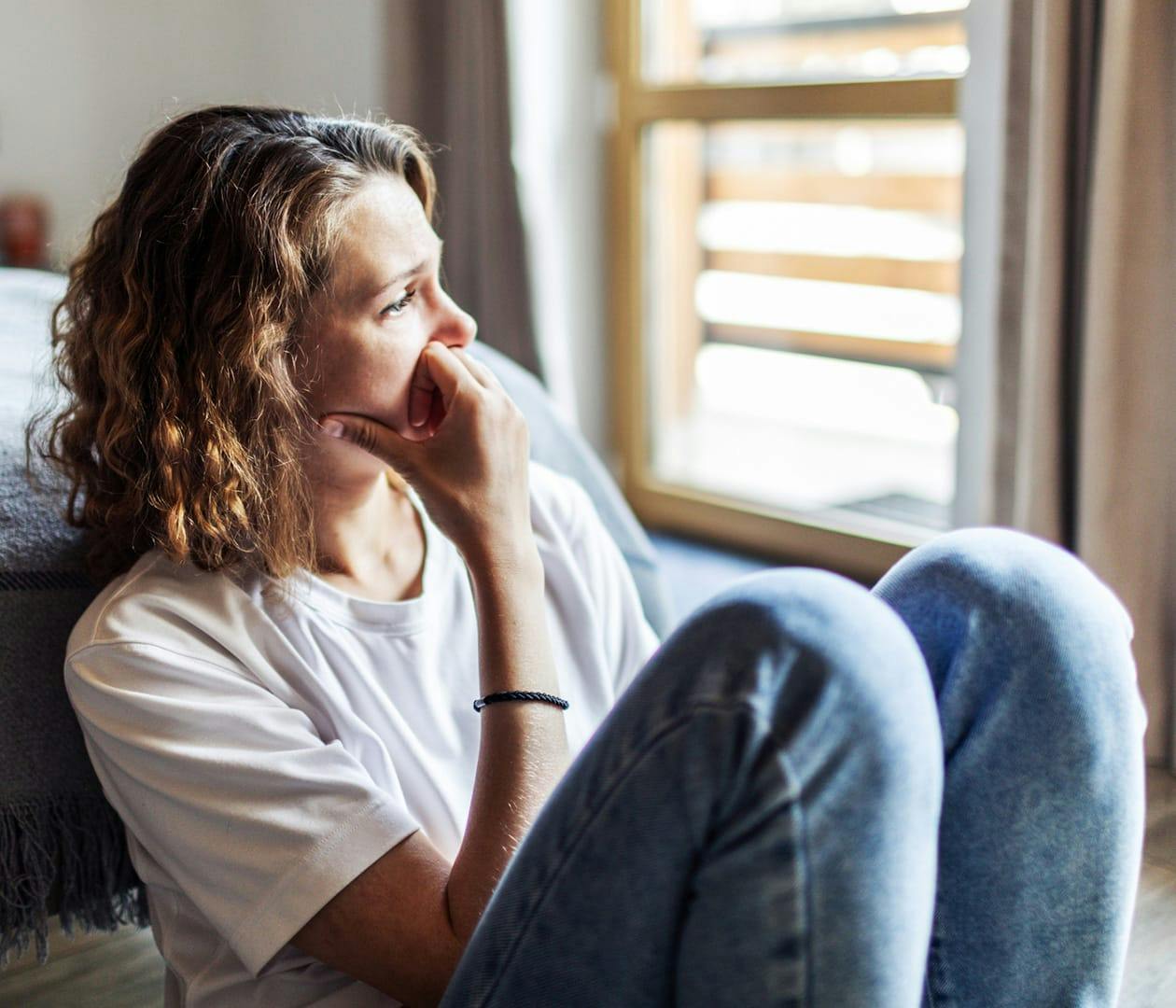 woman sitting down looking out window looking distressed