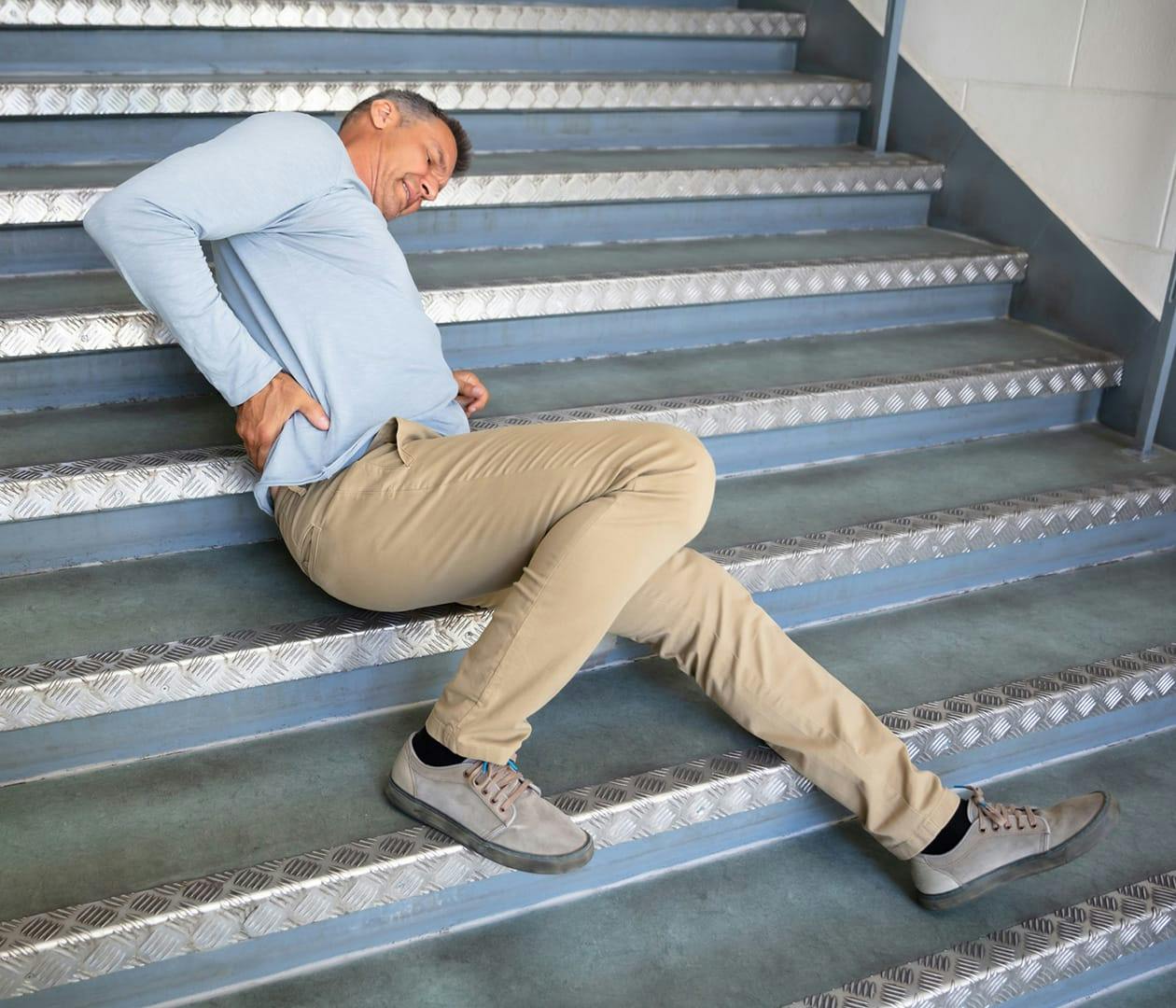 man falling down the stairs holding his lower back