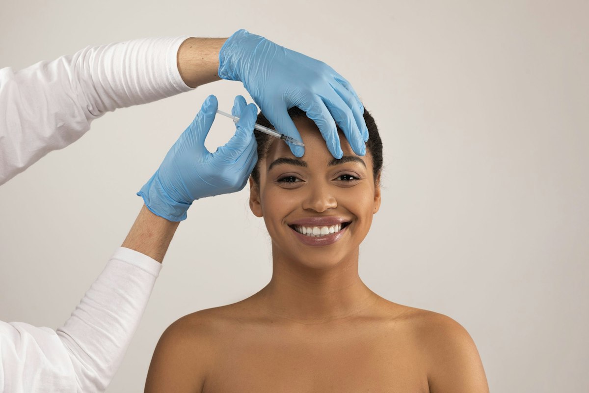 Close-up of a smiling woman receiving a precise forehead Dysport injection from a medical professional wearing blue gloves during a cosmetic treatment in Alpharetta.