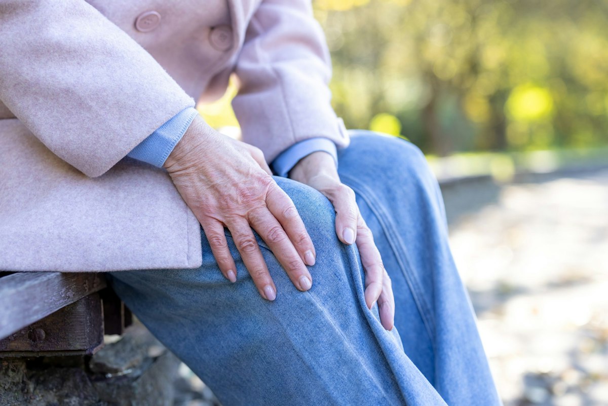 Older woman holding her knee due to arthritis and joint pain while sitting outdoors