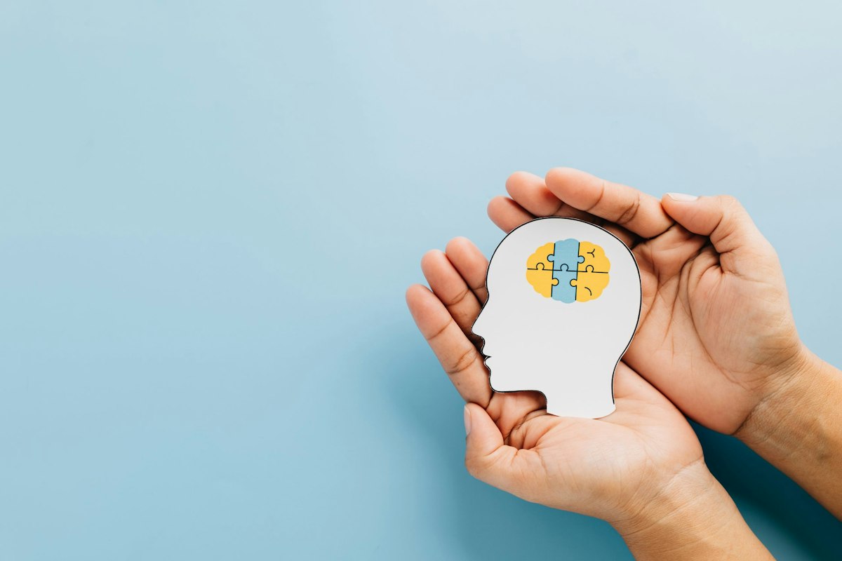Hands holding a head silhouette with a brain illustration representing mental health support and integrated care at Geneva Primary Care in Alpharetta