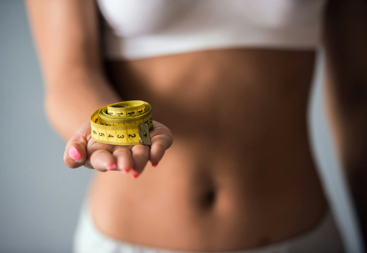 Close-up of a woman holding a yellow measuring tape after starting GLP-1 weight loss injections at Geneva Med Spa in Alpharetta, showing early slimming and body measurement changes.