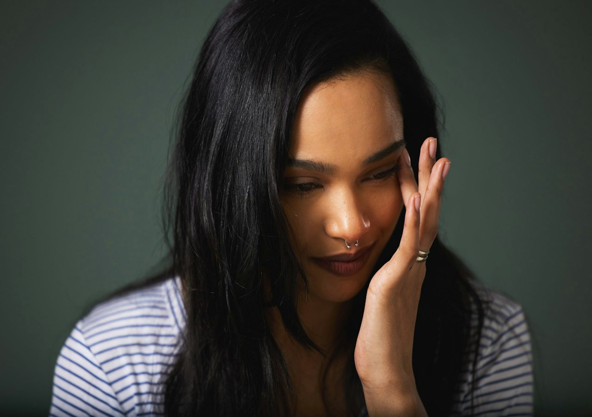 A woman gently touching her face with a tired expression, representing nausea or fatigue that can occur during the early stages of GLP 1 weight loss treatment at Geneva Primary Care and Med Spa in Alpharetta.