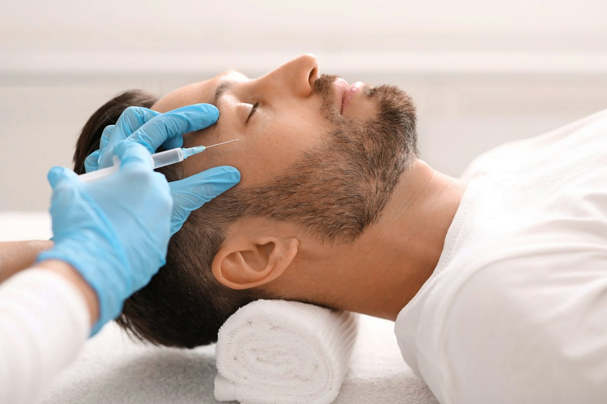 Male patient receiving Botox injections in the forehead area at Geneva Primary Care and Med Spa, administered by a medical provider wearing blue gloves.