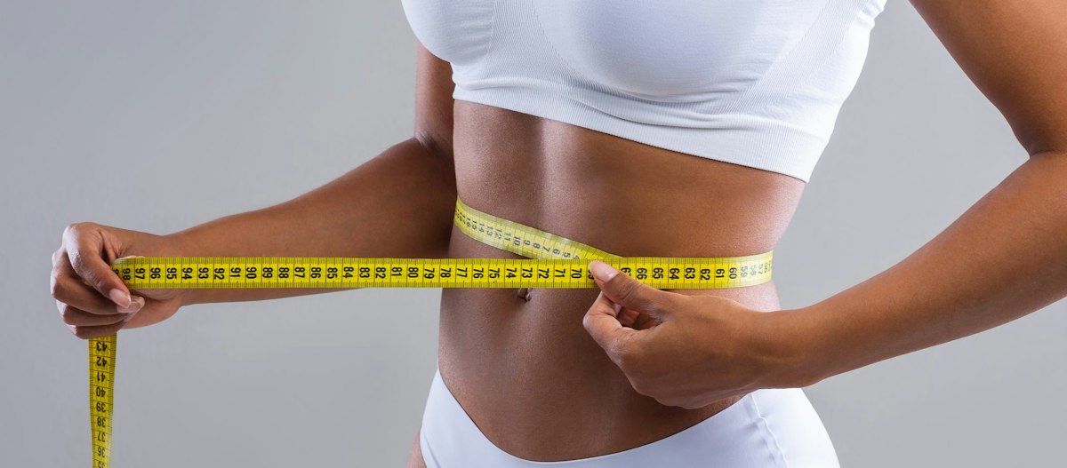 Focused view of a young Black woman checking her waist measurement as part of her fitness and wellness goals at Geneva.