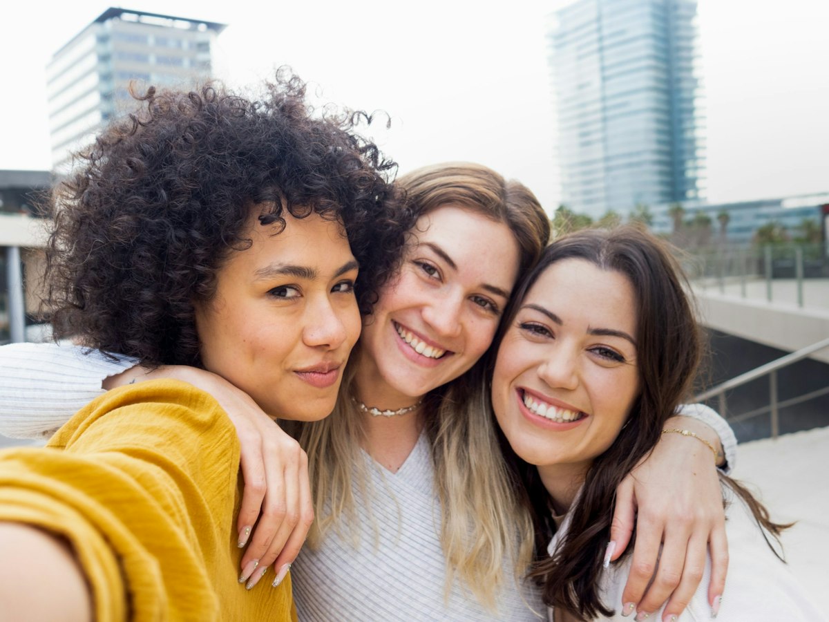 A group of three diverse female friends smiling and taking a selfie together, enjoying friendship and free time.