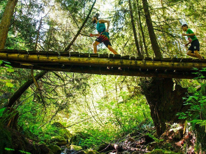 Trail runners crossing a wooden bridge over a stream in a wooded forest