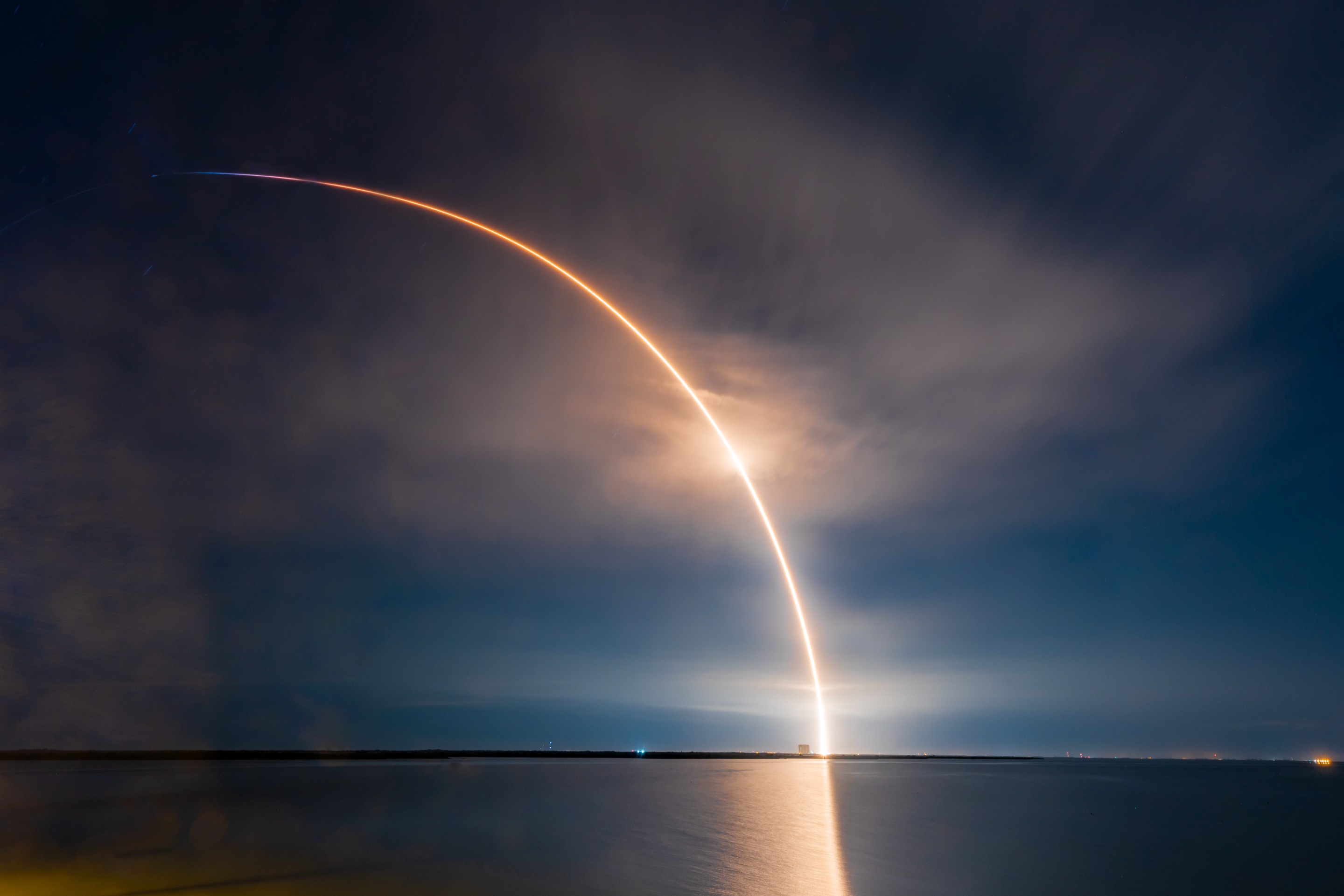 Rocket launch arc over the ocean at night