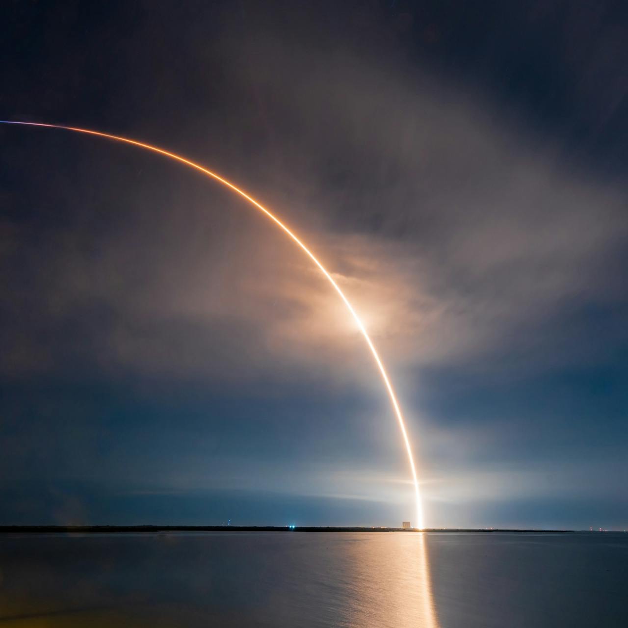 Rocket launch arc over the ocean at night