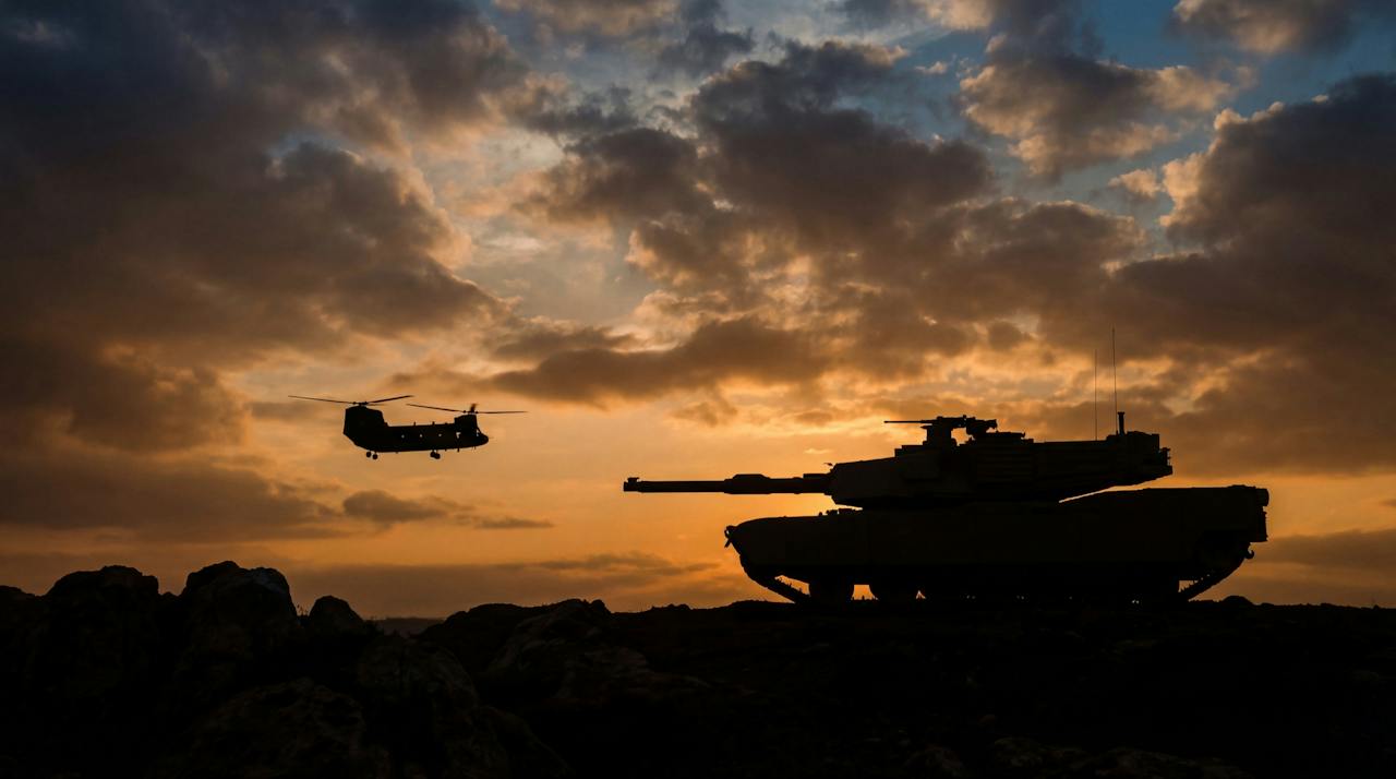 Tank and helicopter silhouetted against a sunset