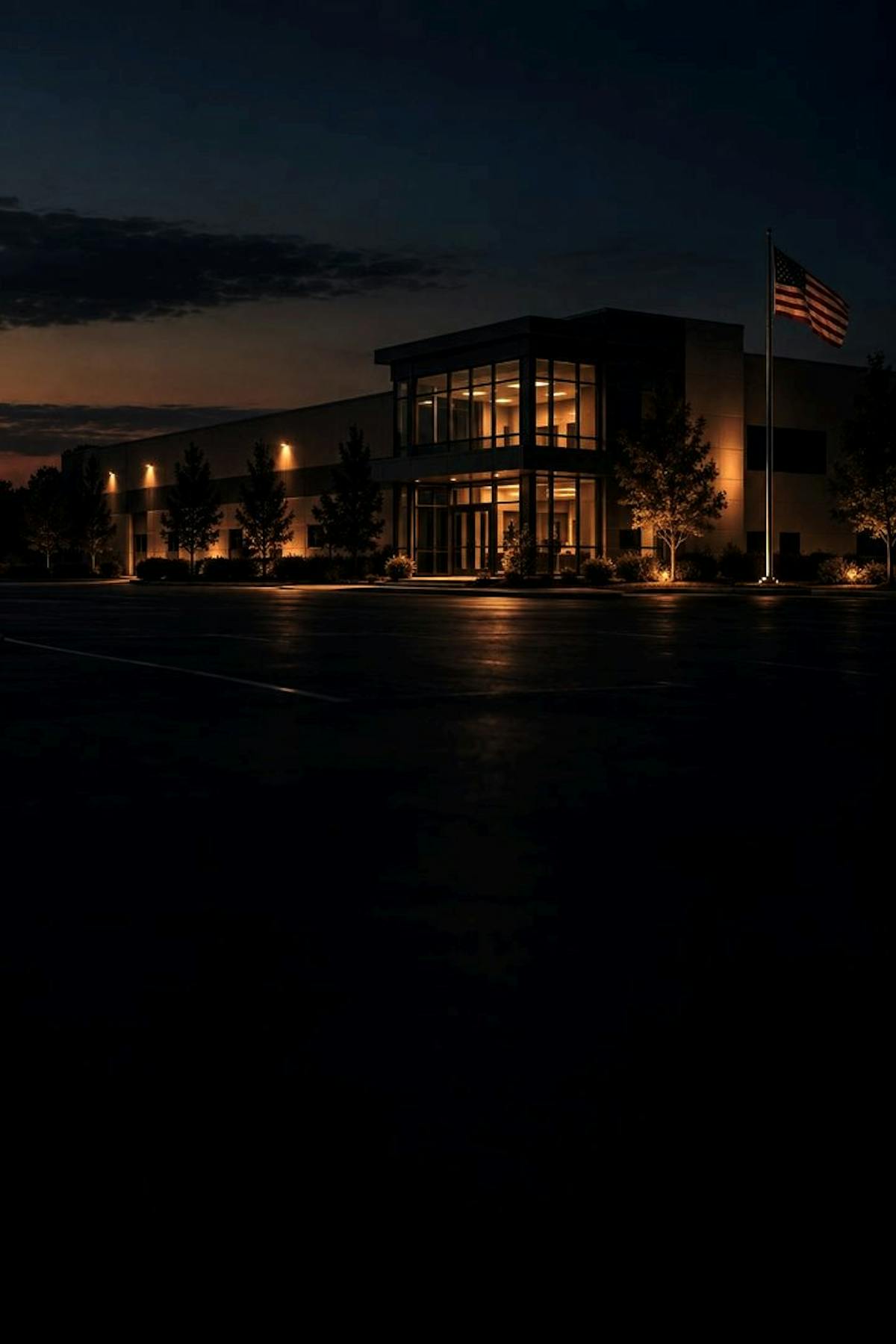 A lit commercial building on an empty lot at dusk, an American flag on the pole