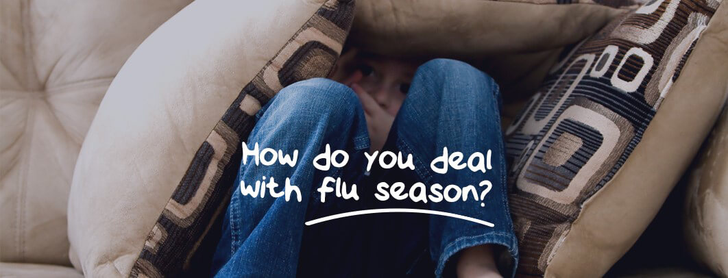 A person is sitting on a beige couch, wearing blue jean, down with flu