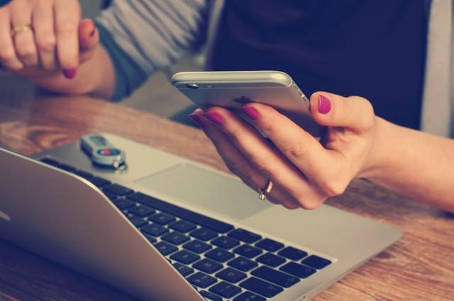 Person sitting at a laptop looking at their iphone