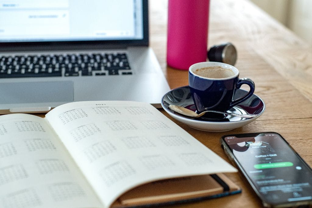 Notice Periods Laptop, coffee cup, and calendar on wooden table.