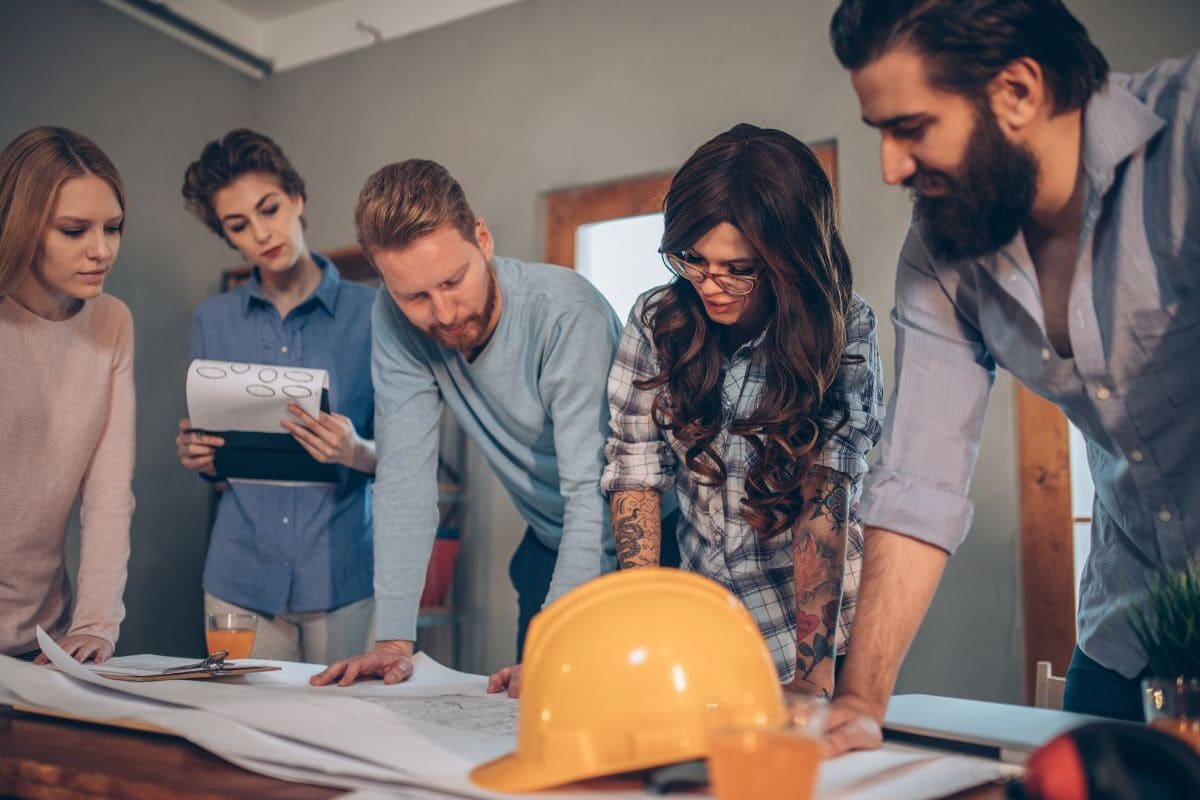 5 people standing over a table working as a team going over building plans