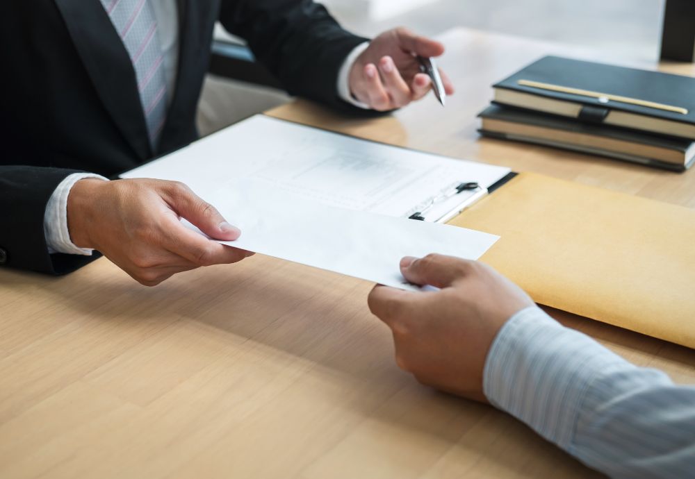 Two people meeting over a desk with one of them handing over resignation letter