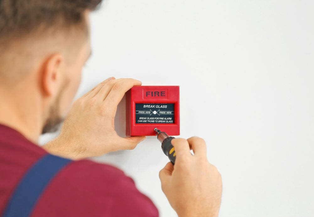 A person installing a fire alarm to comply with new fire regulations