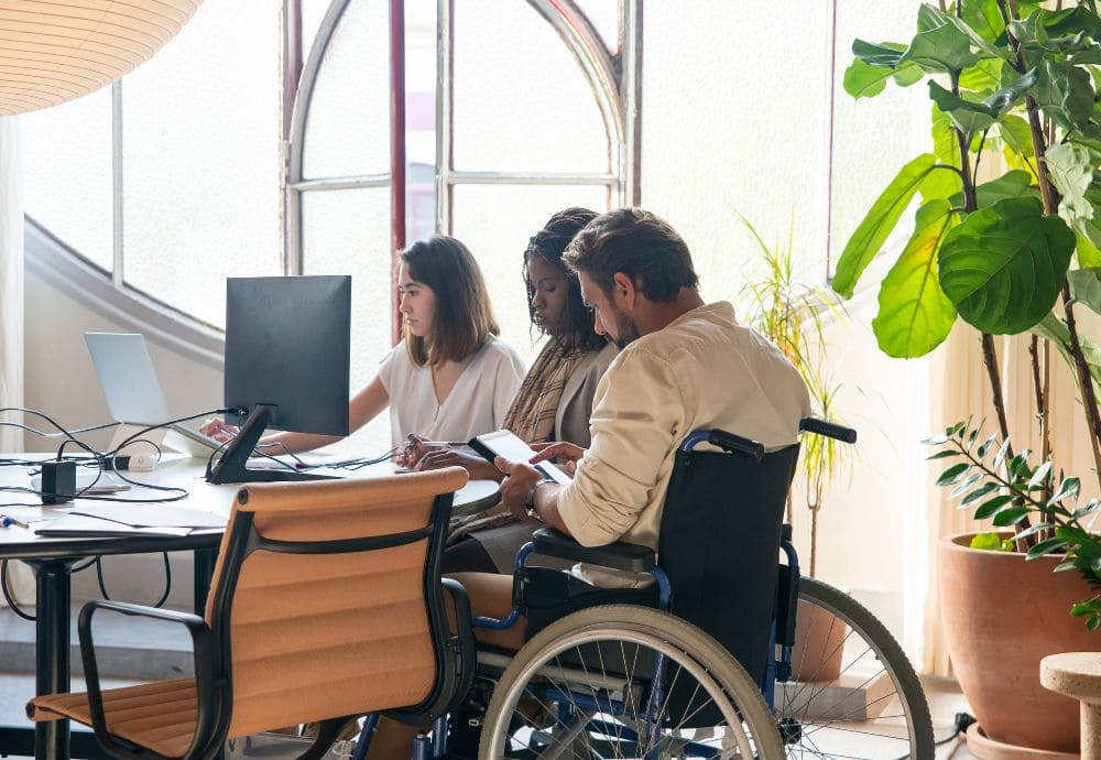 3 people sitting around a desk that has wheelchair accessibility