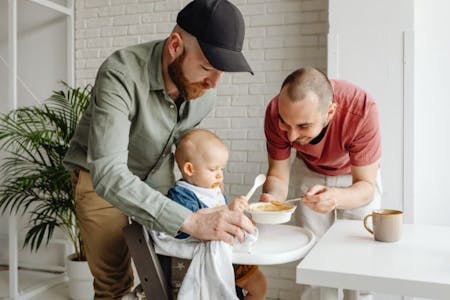 Paternity Leave Same sex couple feeding baby in highchair