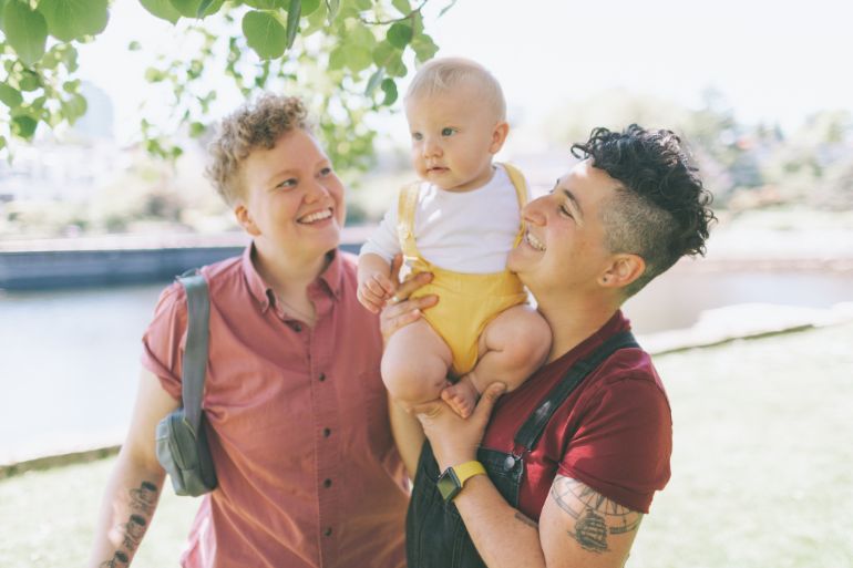 Same sex couple on a walk while lifting their baby