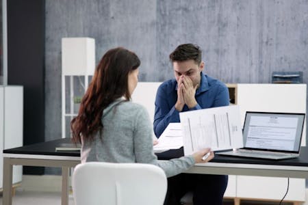 Unauthorized absence A man and woman sitting at a desk with paperwork, facing potential disciplinary action for unauthorized absence.