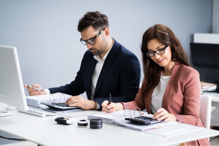 Two colleagues working at a desk in an office, focused on payroll processing