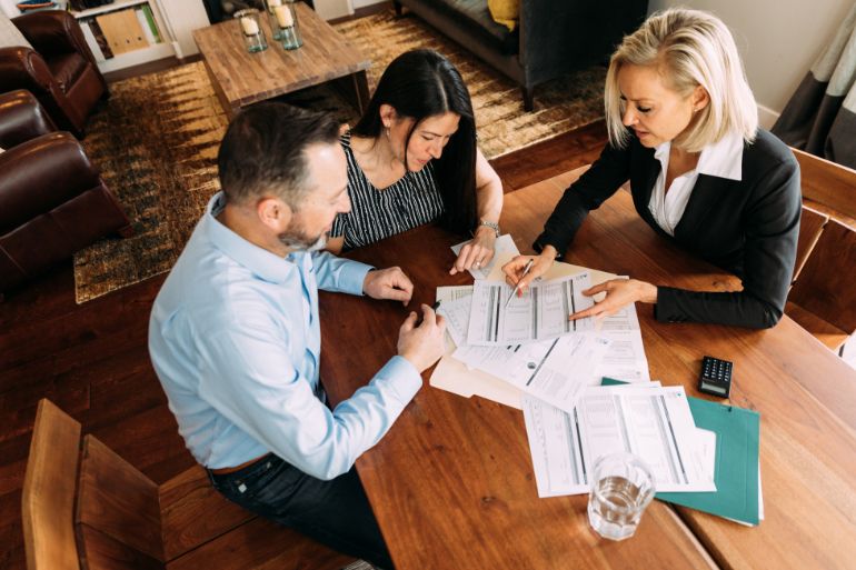 Three people sitting at a table with paperwork, calculating payroll