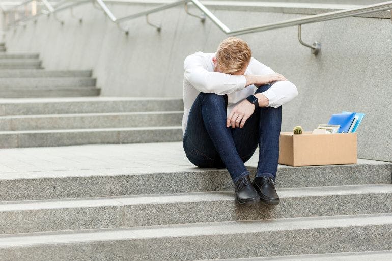 Employee sits on building steps, his head in his hands, grappling with the injustice of unfair dismissal.