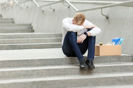 Unfair dismissal Employee sits on building steps, his head in his hands, grappling with the injustice of unfair dismissal.