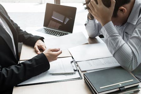 Unfair dismissal An employer and employee sat at a desk discussing an unfair dismissal case.