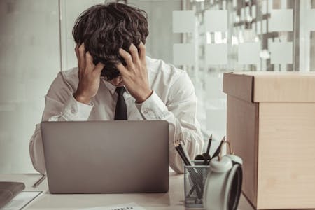 Unfair dismissal A stressed businessman in a suit sits at a desk, his head buried in his hands, reflecting unfair dismissal