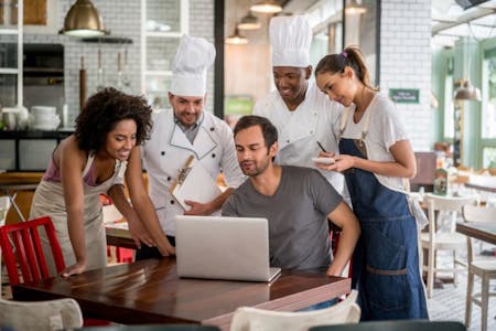 Rota planning Business owner and staff collaborating on a laptop in a restaurant, focusing on rota planning.
