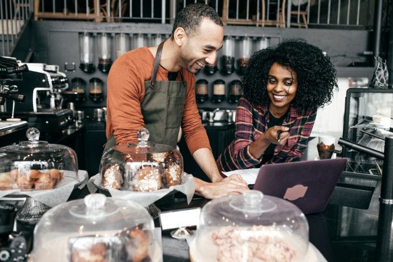 Business owners working on a laptop in their coffee shop using small business payroll software.