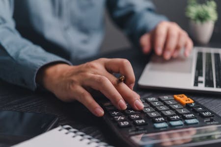 Person using calculator on desk with laptop, manually processing payroll.